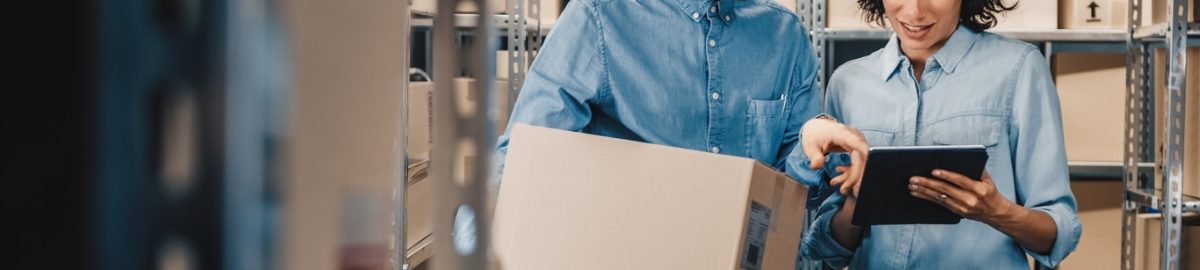 Female Inventory Manager Shows Digital Tablet Information to a Worker Holding Cardboard Box, They Talk and Do Work. In the Background Stock of Parcels with Products Ready for Shipment.